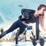 Woman performing a plank row with dumbbells in a bright Dubai gym.