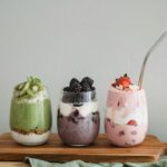 Colorful homemade fruit smoothies with kiwi, blackberry, and strawberry on a wooden board.