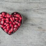 Delicious and juicy pomegranate seeds in a heart-shaped bowl on a wooden table.